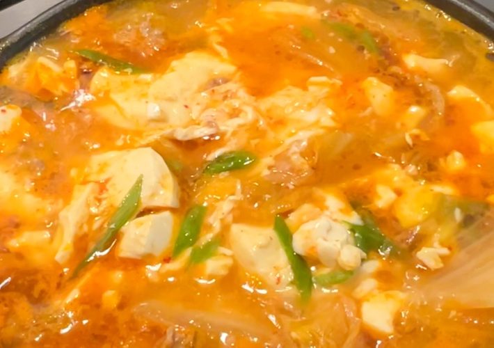 Kimchi soft tofu stew with pork, egg, and green onions bubbling in a pot