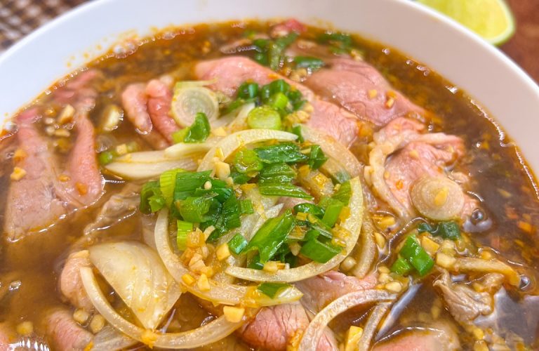 Weeknight bún bò Huế noodle soup with thin ribeye, green onions and onion garnish