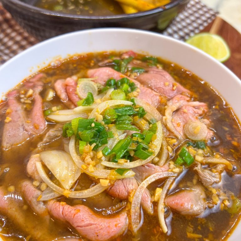 Weeknight bún bò Huế noodle soup with thin ribeye, green onions and onion garnish