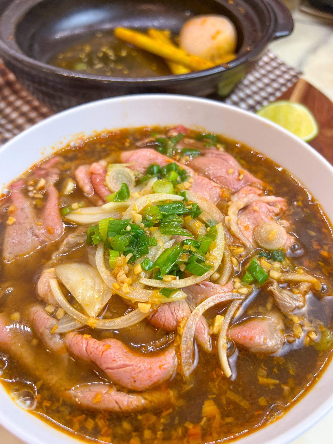 Bowl of weeknight bún bò Huế with sliced ribeye, onion, green onions, and chewy noodles