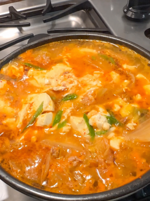 Kimchi soft tofu stew with pork and egg bubbling in a pot on a clean stovetop