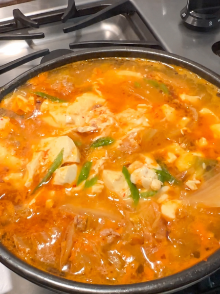 Kimchi soft tofu stew with pork and egg bubbling in a pot on a clean stovetop