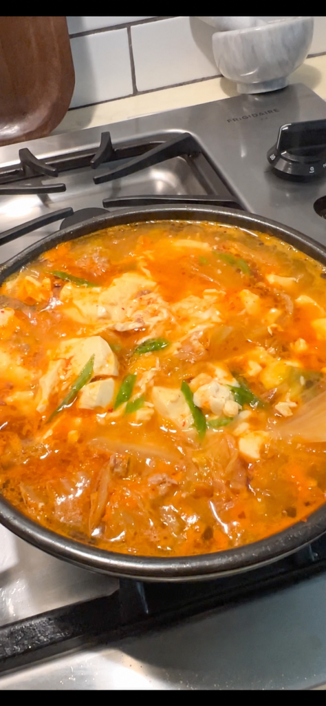 Kimchi soft tofu stew with pork and egg bubbling in a pot on a clean stovetop