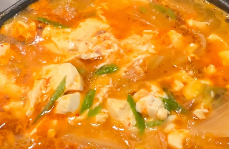 Kimchi soft tofu stew with pork and egg bubbling in a pot on a clean stovetop