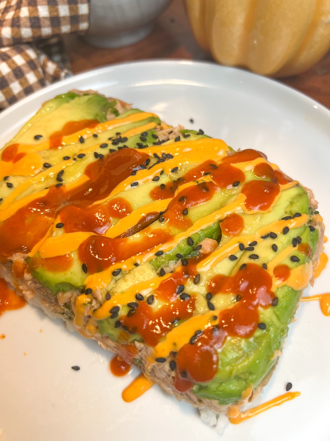 Close-up of an air fryer salmon stack layered with avocado and sushi rice, topped with spicy mayo, Sriracha, and black sesame seeds.