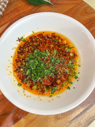 Chili crisp bread dipping oil with scallions, sesame seeds, and cilantro in a white bowl