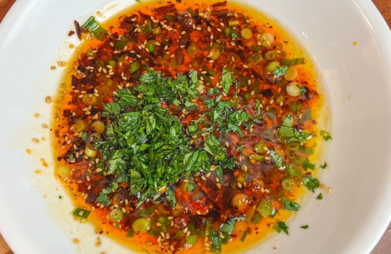 Chili crisp bread dipping oil with scallions, sesame seeds, and cilantro in a white bowl