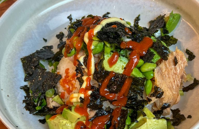Smoked salmon rice bowl topped with avocado, edamame, Kewpie mayo, sriracha, and crumbled roasted seaweed.