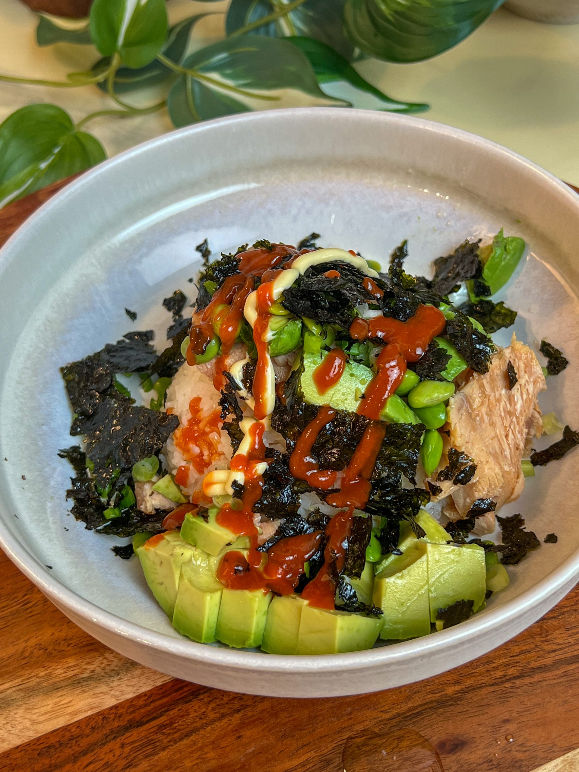 Smoked salmon rice bowl topped with avocado, edamame, Kewpie mayo, sriracha, and crumbled roasted seaweed.