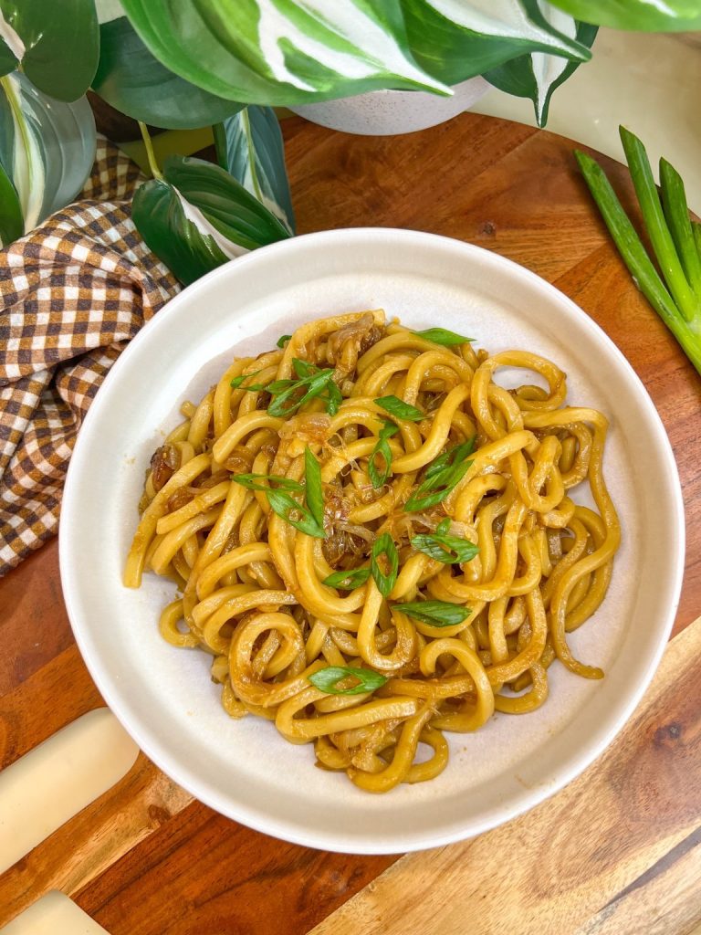Caramelized shallot udon noodles topped with sliced green onions in a white bowl