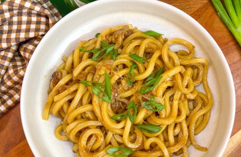 Caramelized shallot udon noodles topped with sliced green onions in a white bowl