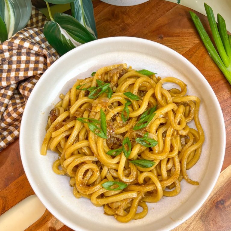 Caramelized shallot udon noodles topped with sliced green onions in a white bowl