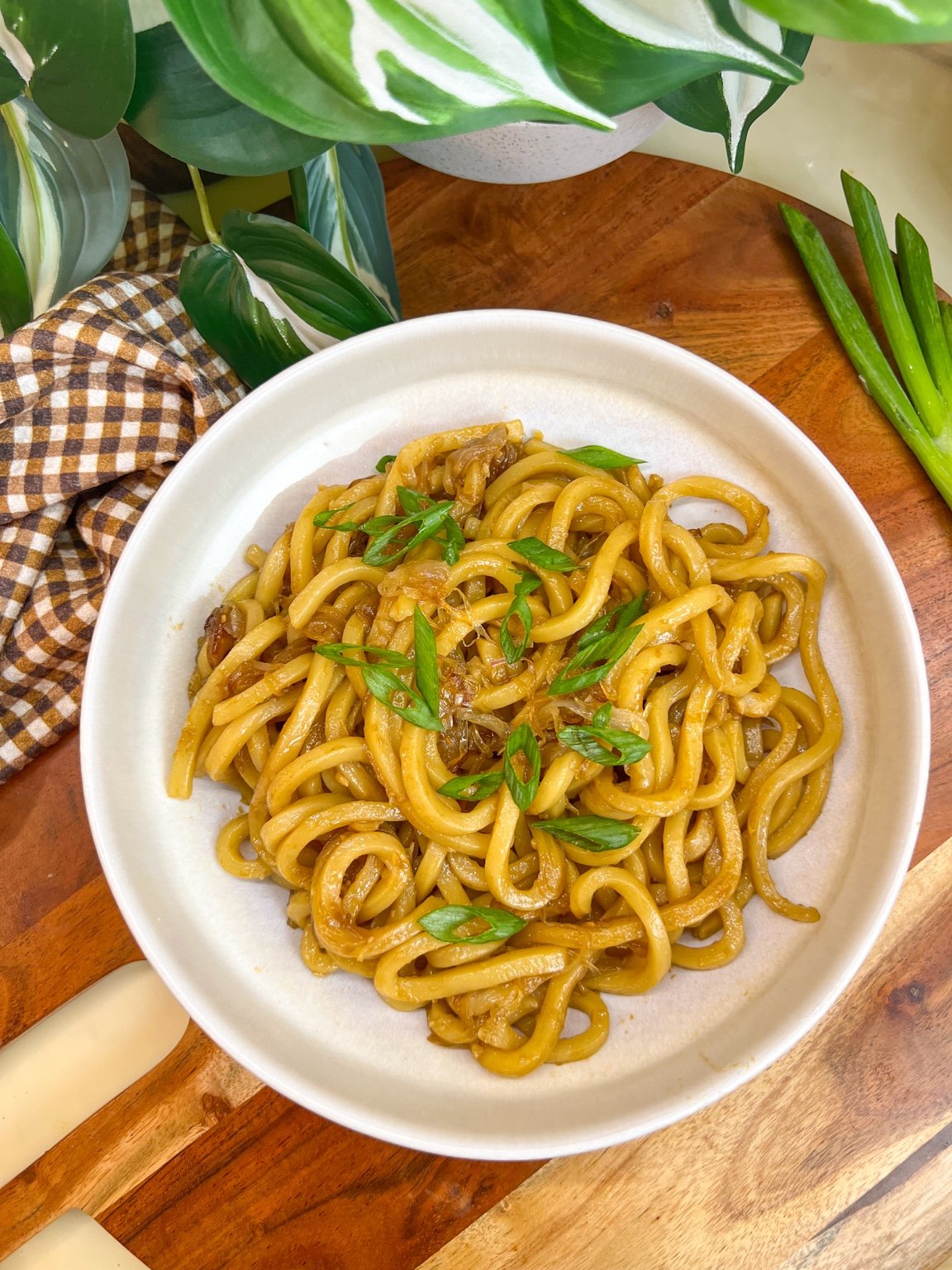 Caramelized shallot udon noodles topped with sliced green onions in a white bowl